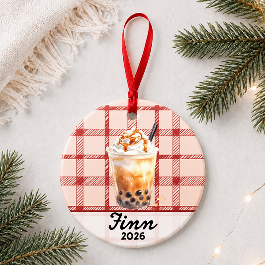 Personalized brown sugar boba ceramic ornament with name and year on red plaid styled with pine branches on a soft white background