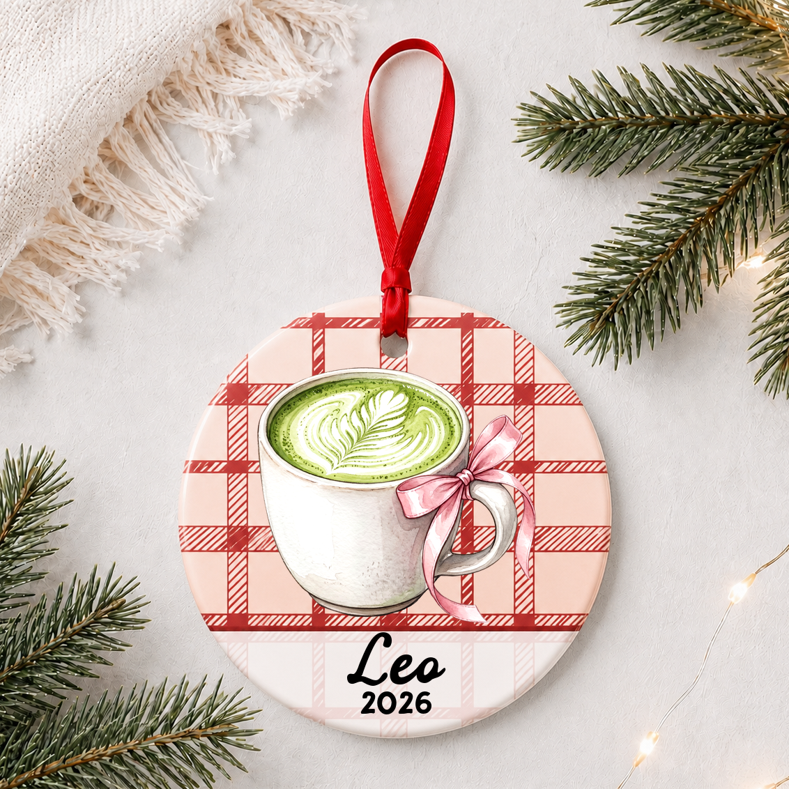 Personalized matcha latte ceramic ornament with name and year on red plaid styled with pine branches on a soft white background