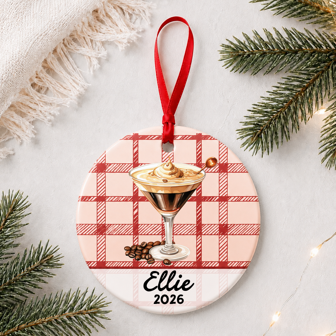 Personalized espresso martini ceramic ornament with name and year on red plaid styled with pine branches on a soft white background