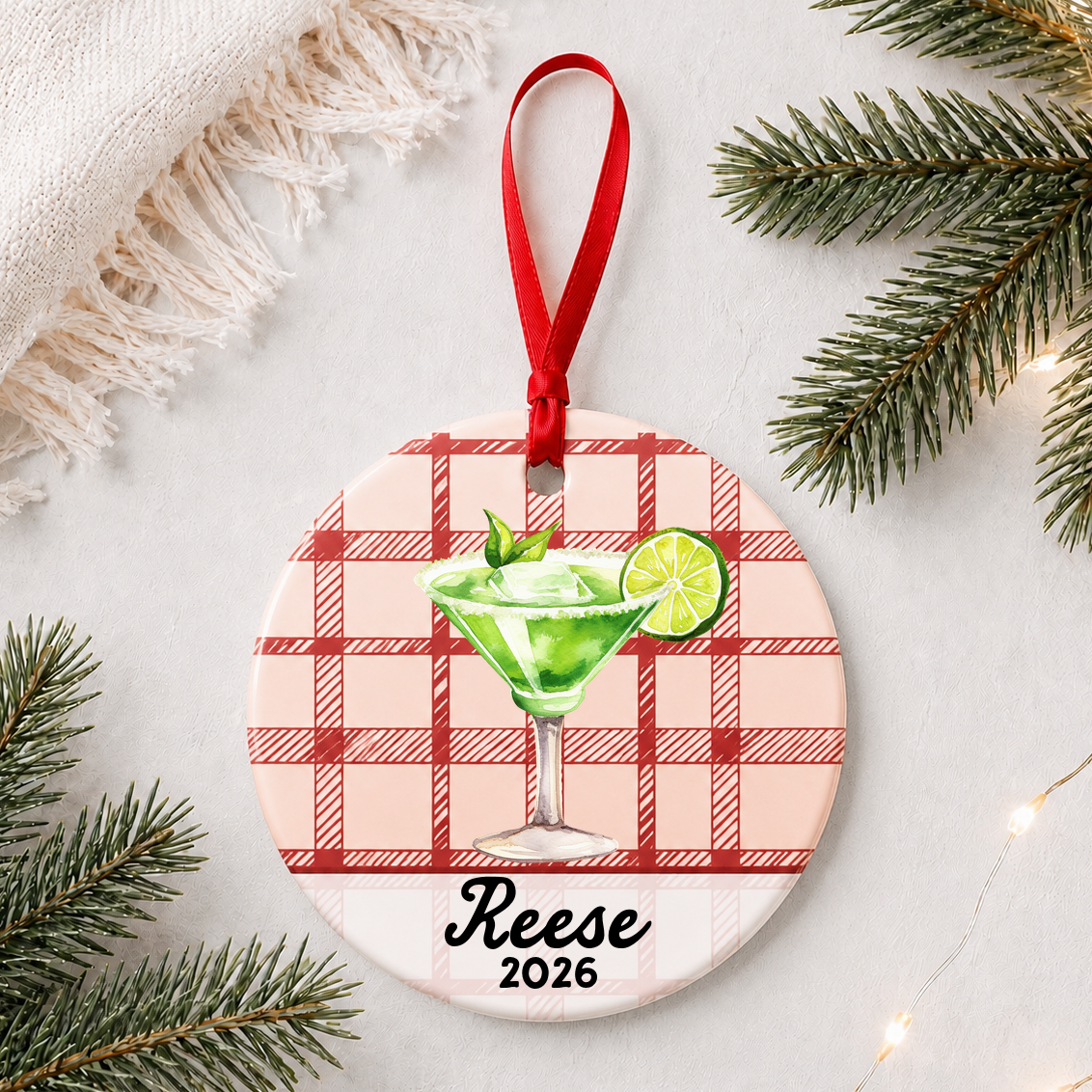 Personalized margarita ceramic ornament with name and year on red plaid styled with pine branches on a soft white background