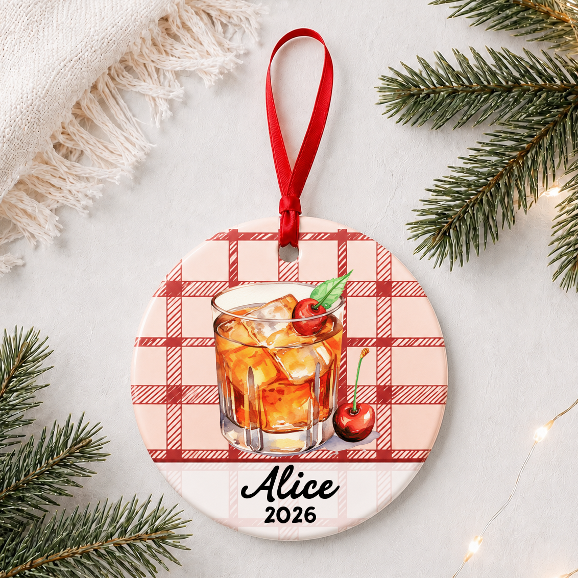 Personalized Old Fashioned cocktail ceramic ornament with name and year on red plaid styled with pine branches on a soft white background