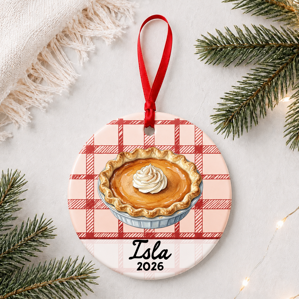 Personalized pumpkin pie ceramic ornament with name and year on red plaid styled with pine branches on a soft white background
