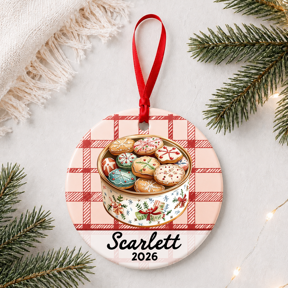 Personalized Christmas cookie tin ceramic ornament with name and year on red plaid styled with pine branches on a soft white background