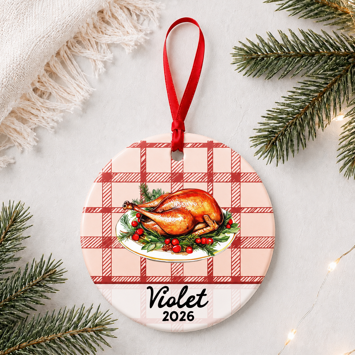 Personalized roast turkey ceramic ornament with name and year on red plaid styled with pine branches on a soft white background