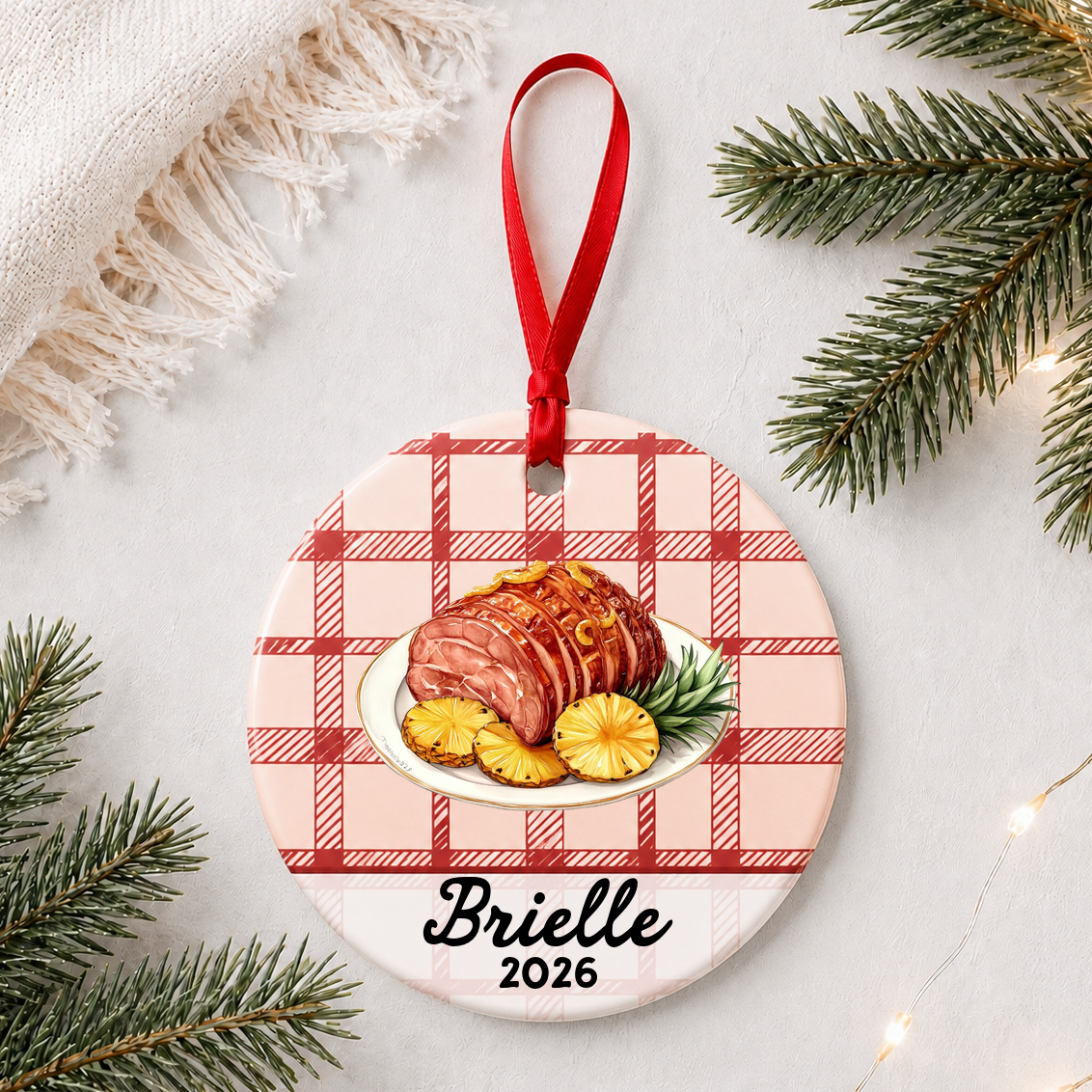 Personalized Christmas ham ceramic ornament with name and year on red plaid styled with pine branches on a soft white background
