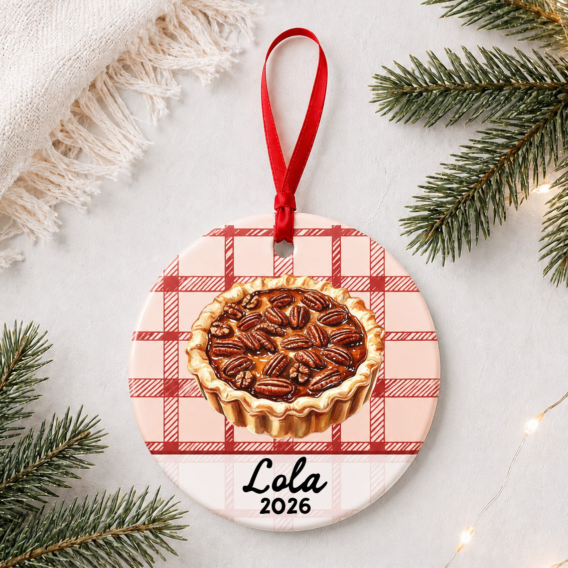 Personalized pecan pie ceramic ornament with name and year on red plaid styled with pine branches on a soft white background