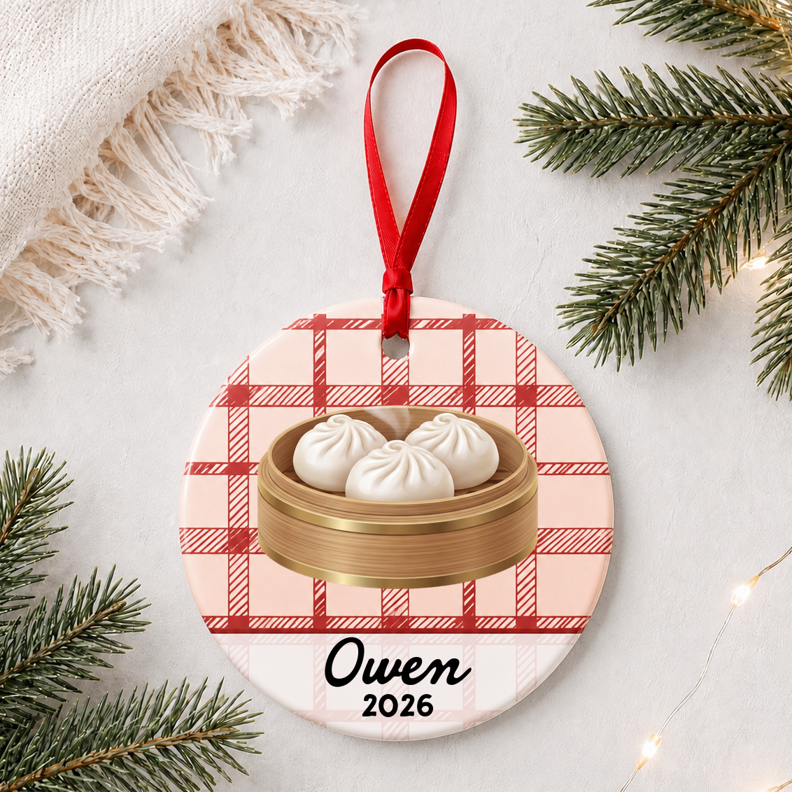 Personalized soup dumpling ceramic ornament with name and year on red plaid styled with pine branches on a soft white background