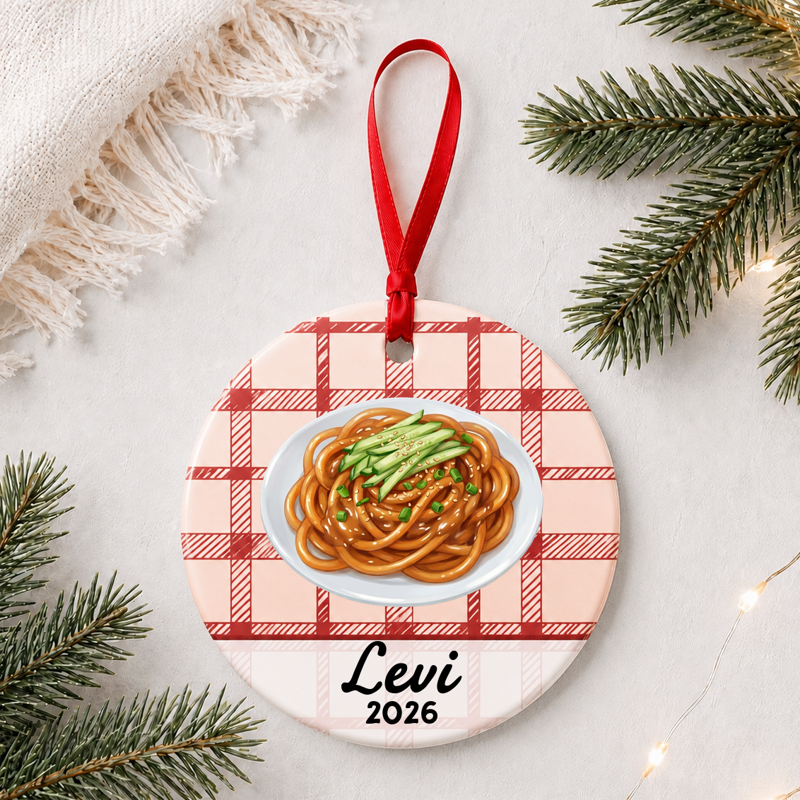 Personalized sesame noodles ceramic ornament with name and year on red plaid styled with pine branches on a soft white background
