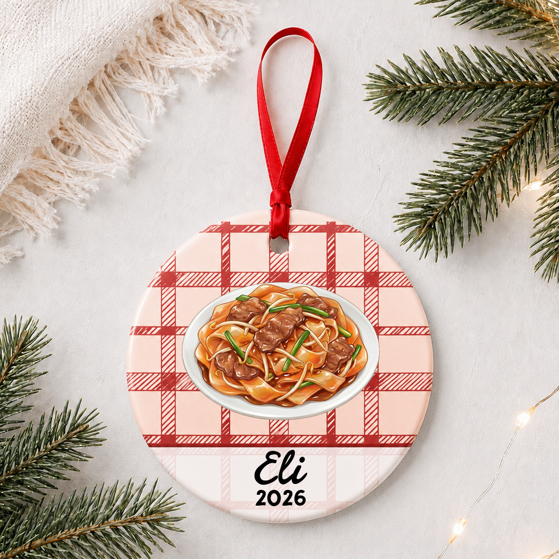 Personalized beef chow fun ceramic ornament with name and year on red plaid styled with pine branches on a soft white background