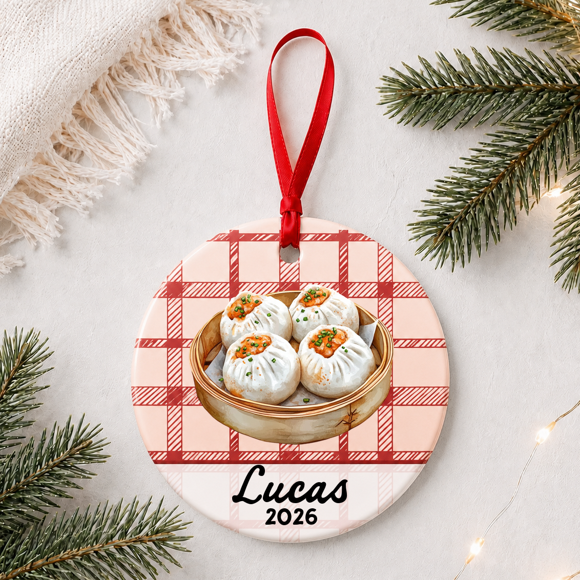 Personalized shumai ceramic ornament with name and year on red plaid styled with pine branches on a soft white background