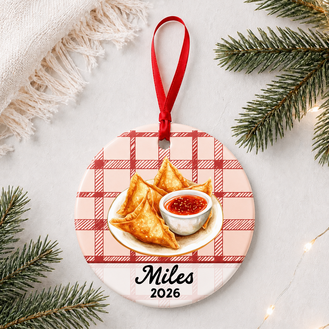 Personalized crab rangoon ceramic ornament with name and year on red plaid styled with pine branches on a soft white background