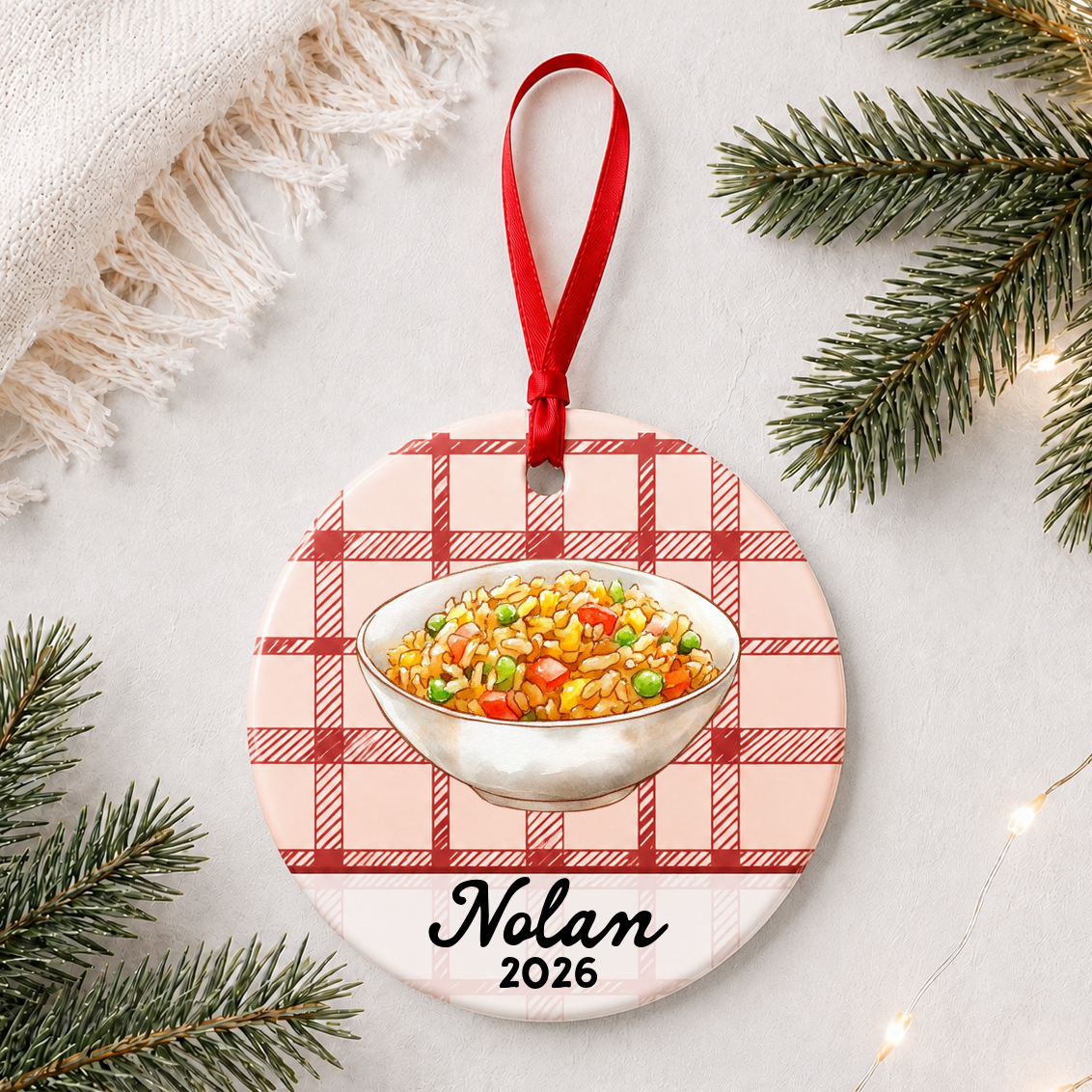 Personalized fried rice ceramic ornament with name and year on red plaid styled with pine branches on a soft white background