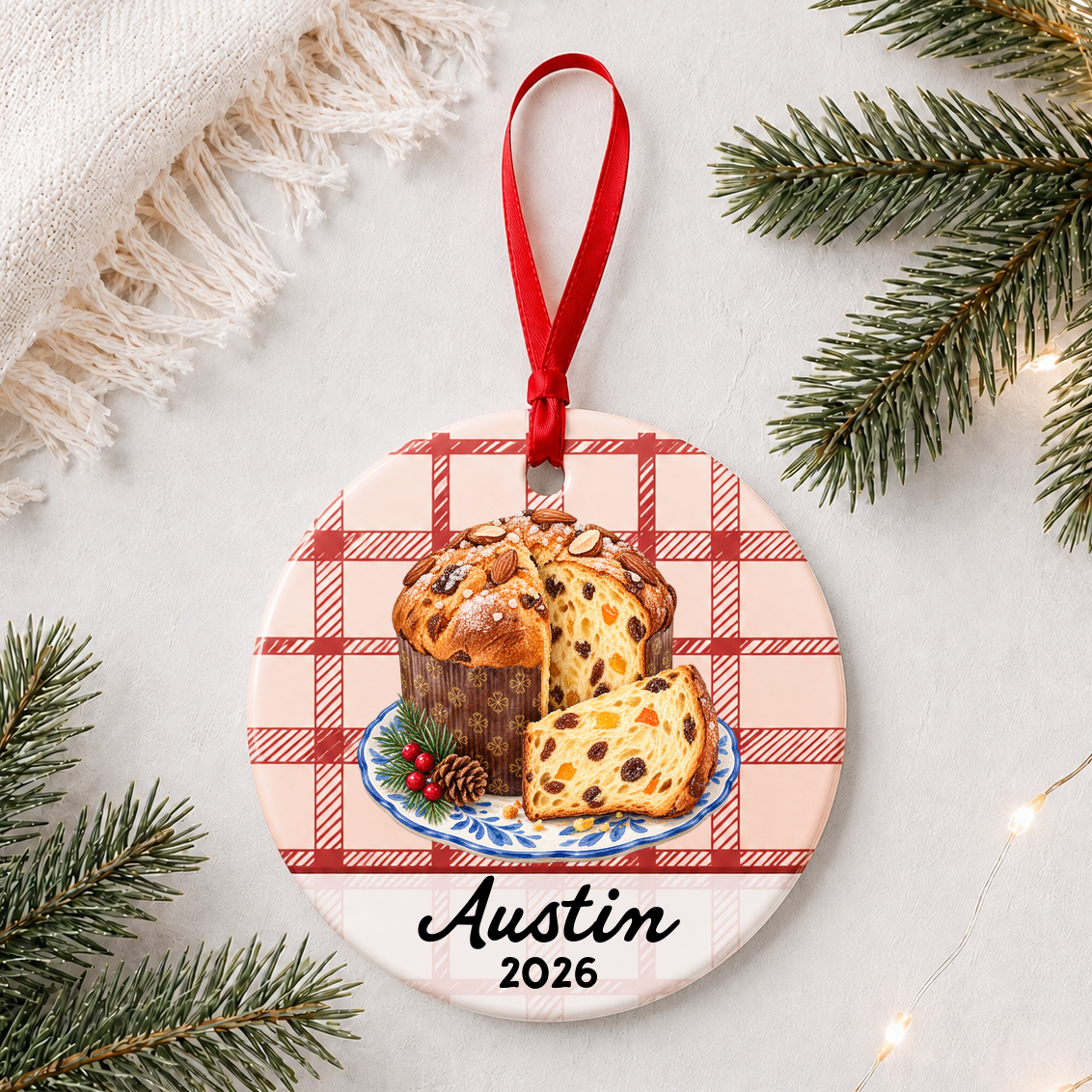 Personalized panettone ceramic ornament with name and year on red plaid styled with pine branches on a soft white background