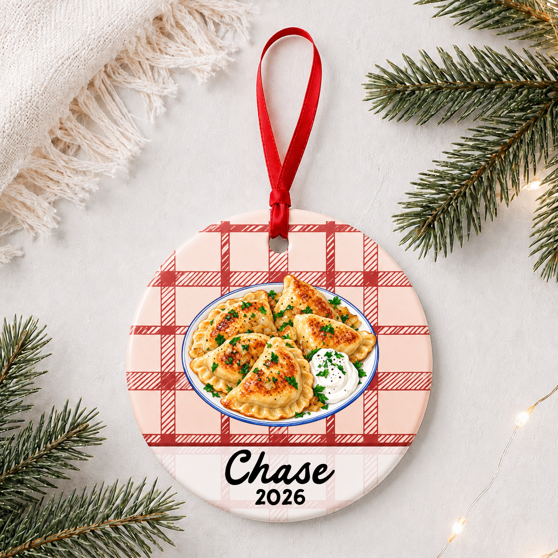 Personalized pierogi ceramic ornament with name and year on red plaid styled with pine branches on a soft white background