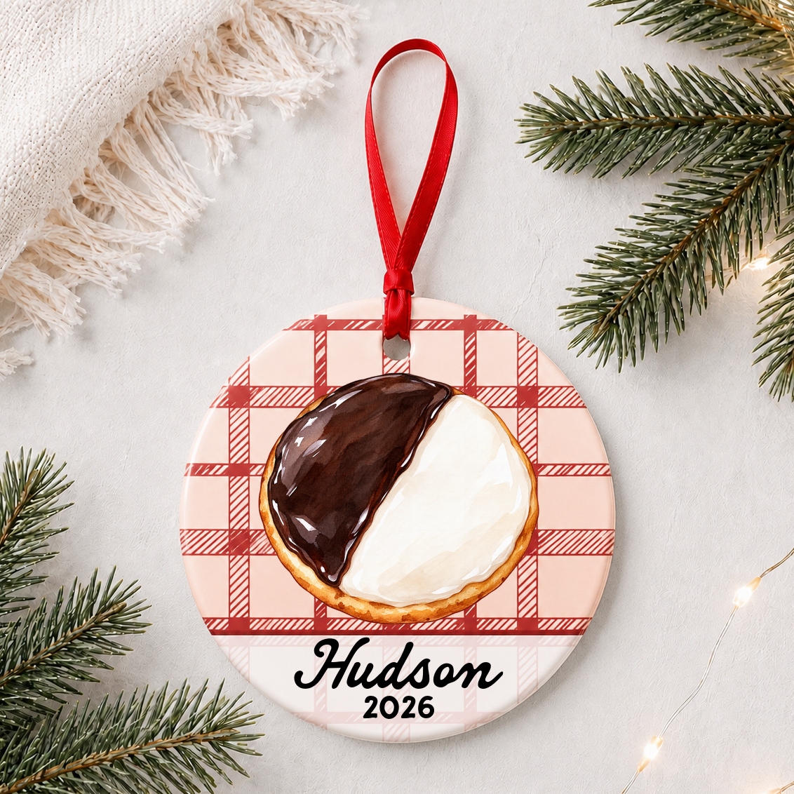 Personalized black and white cookie ceramic ornament with name and year on red plaid styled with pine branches on a soft white background