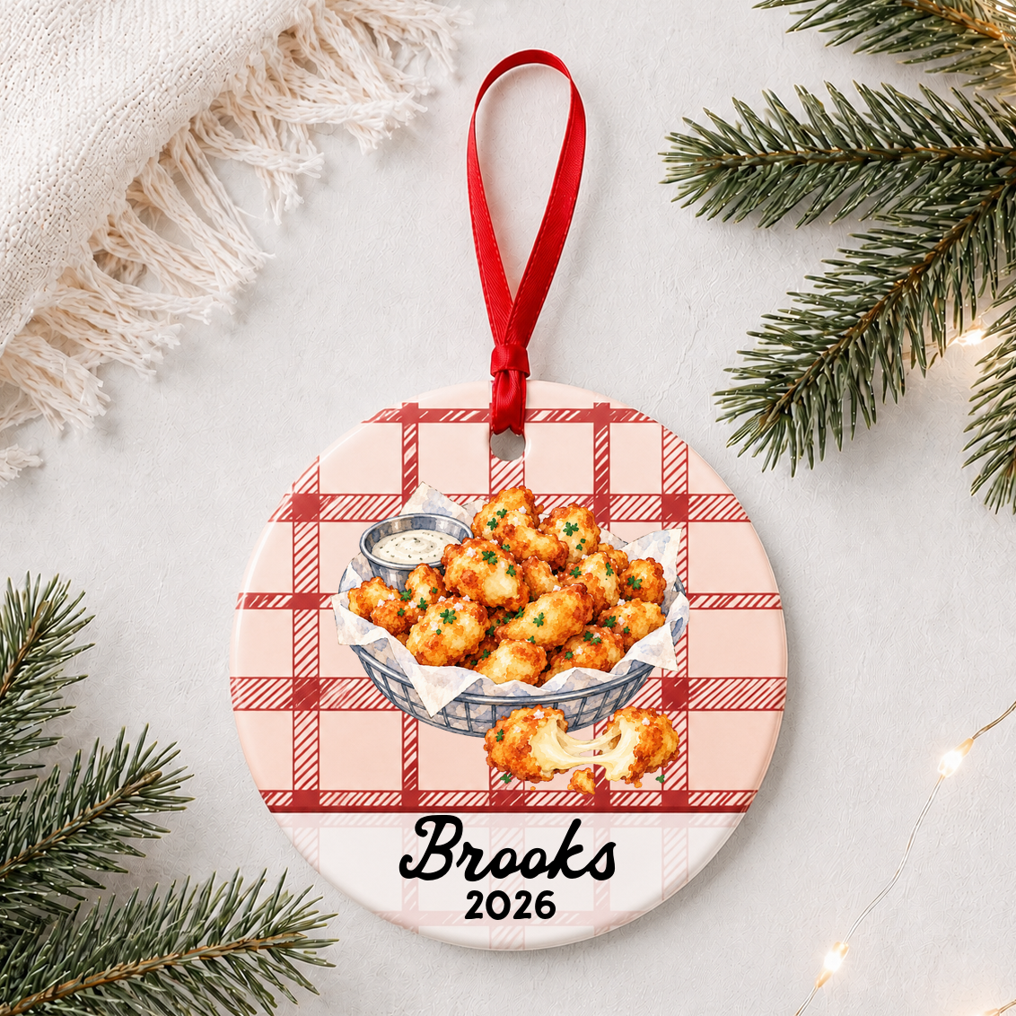 Personalized cheese curds ceramic ornament with name and year on red plaid styled with pine branches on a soft white background