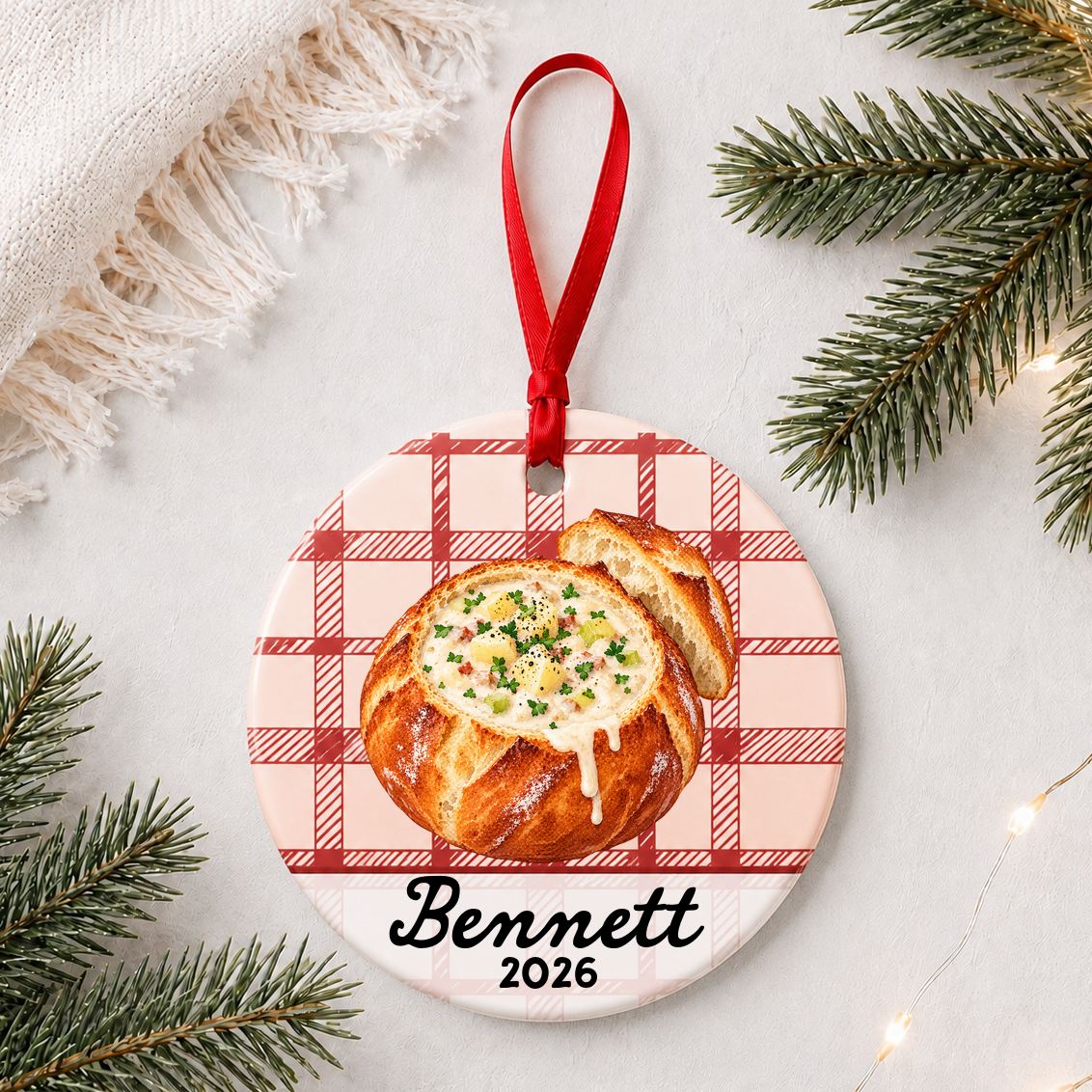 Personalized clam chowder bread bowl ceramic ornament with name and year on red plaid styled with pine branches on a soft white background