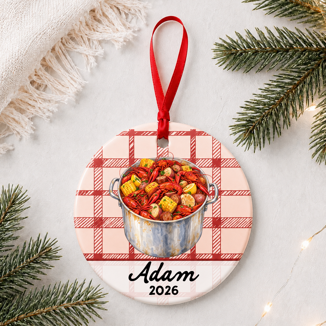 Personalized crawfish boil ceramic ornament with name and year on red plaid styled with pine branches on a soft white background