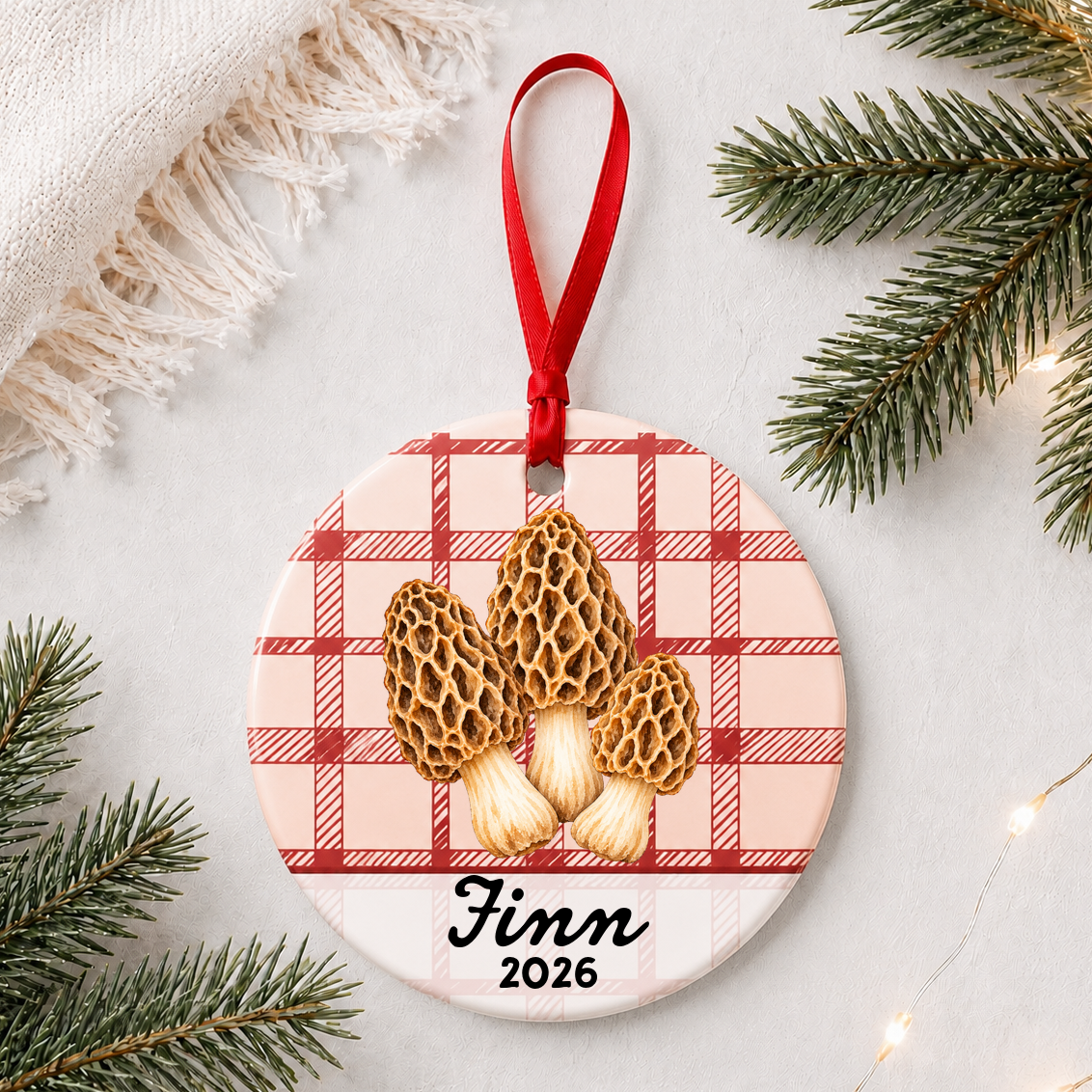 Personalized morel mushrooms ceramic ornament with name and year on red plaid styled with pine branches on a soft white background