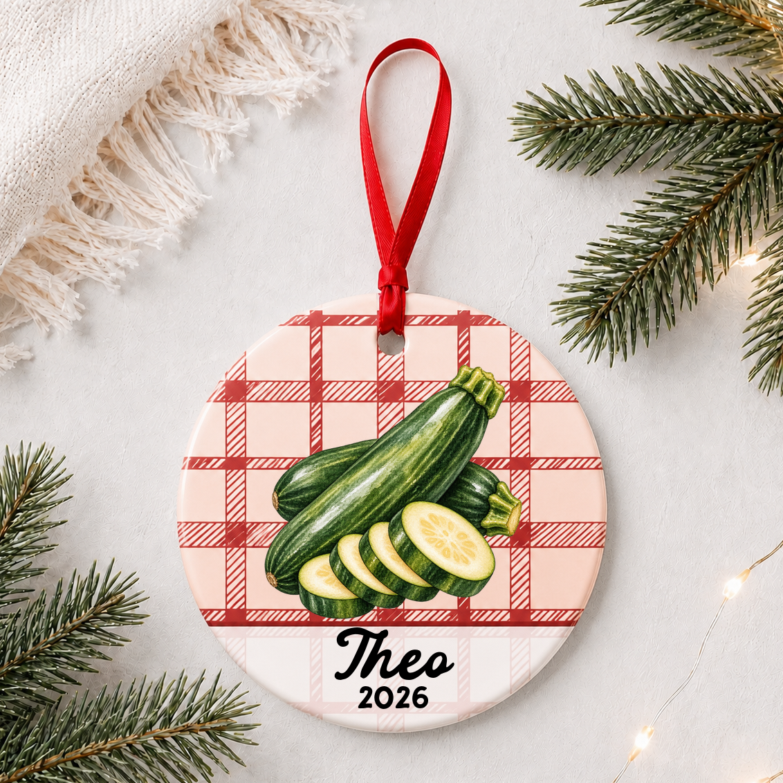 Personalized zucchini ceramic ornament with name and year on red plaid styled with pine branches on a soft white background
