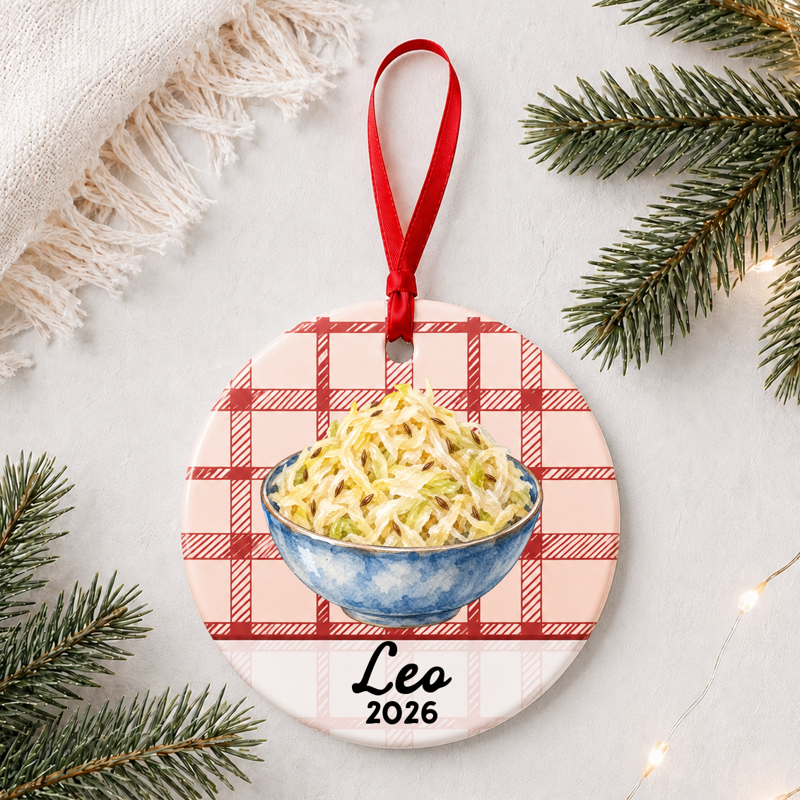 Personalized sauerkraut ceramic ornament with name and year on red plaid styled with pine branches on a soft white background