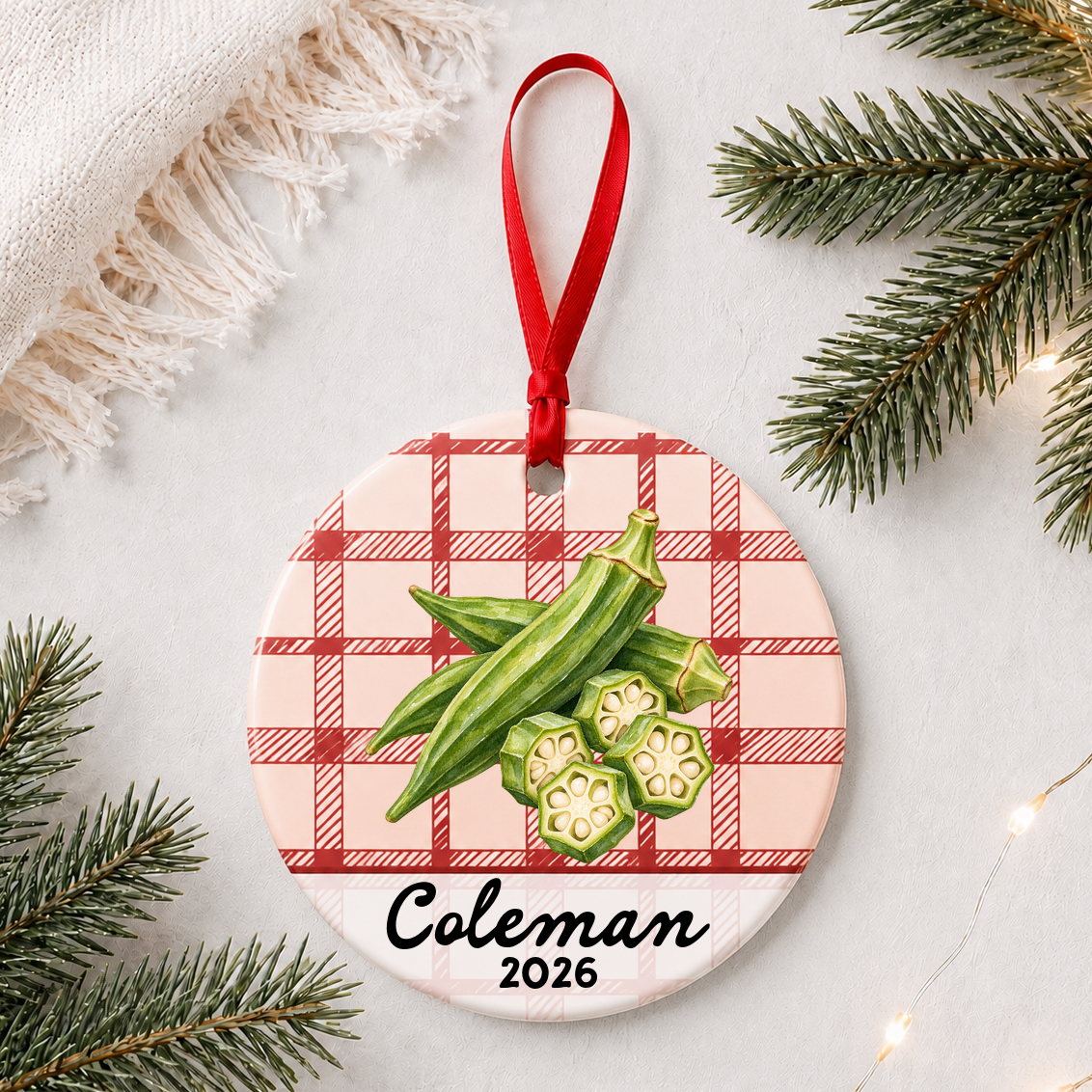 Personalized okra ceramic ornament with name and year on red plaid styled with pine branches on a soft white background