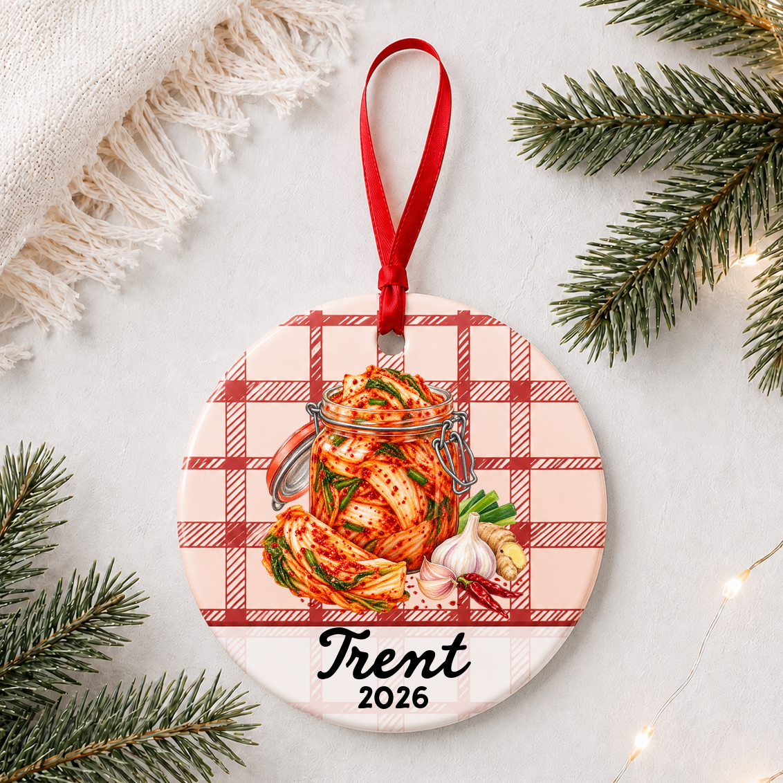 Personalized kimchi ceramic ornament with name and year on red plaid styled with pine branches on a soft white background