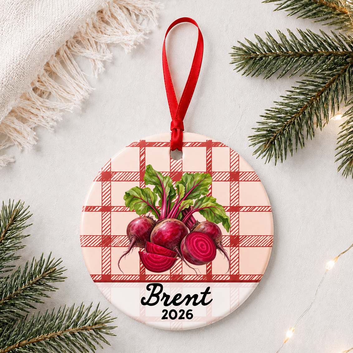 Personalized beets ceramic ornament with name and year on red plaid styled with pine branches on a soft white background