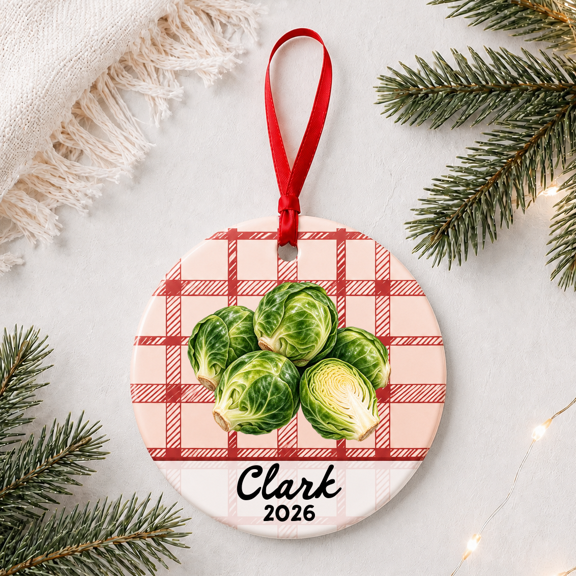 Personalized brussels sprouts ceramic ornament with name and year on red plaid styled with pine branches on a soft white background