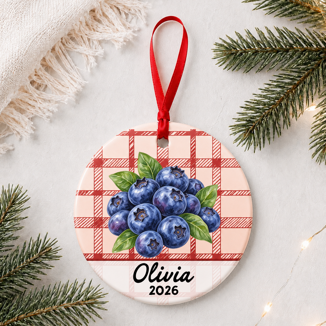 Personalized blueberries ceramic ornament with name and year on red plaid styled with pine branches on a soft white background