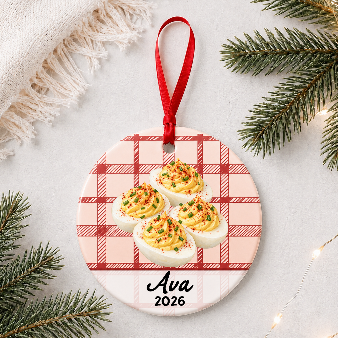 Personalized deviled eggs ceramic ornament with name and year on red plaid styled with pine branches on a soft white background
