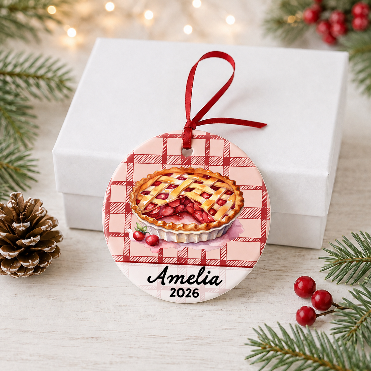 Personalized cherry pie ceramic ornament displayed in front of a white gift box with holiday greenery