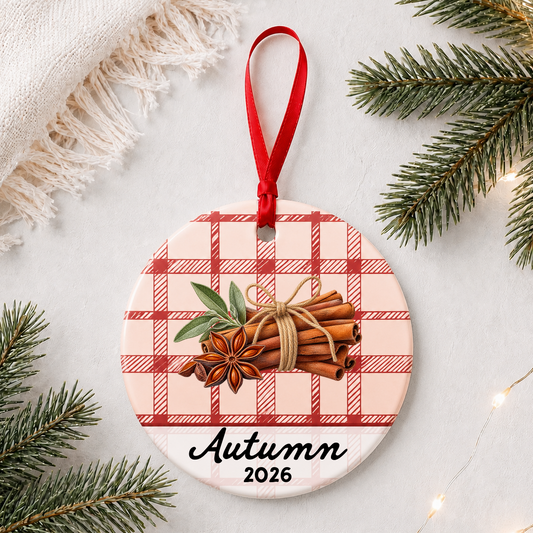 Personalized cinnamon stick ceramic ornament with name and year on red plaid styled with pine branches on a soft white background