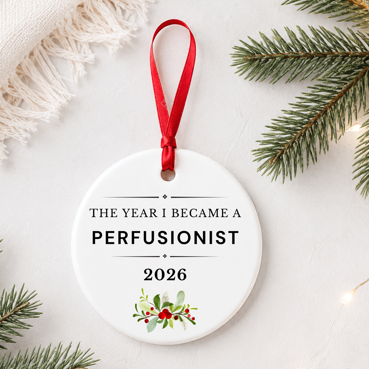 Perfusionist 2026 ceramic ornament reading The Year I Became a Perfusionist styled with pine branches on a soft white background
