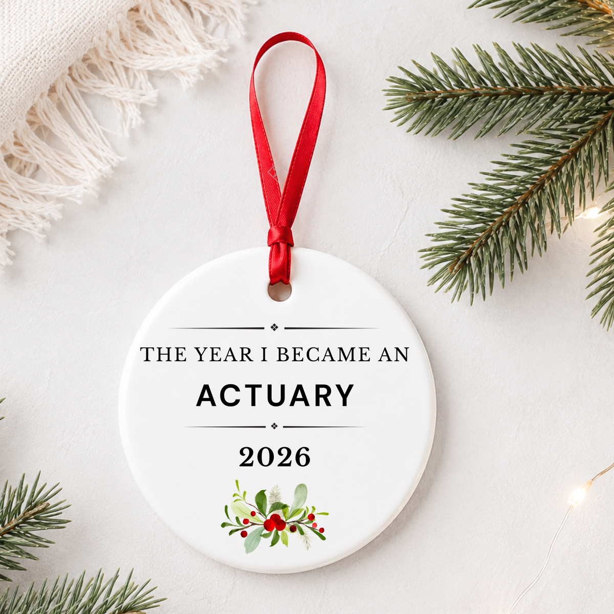 Actuary 2026 ceramic ornament reading The Year I Became an Actuary styled with pine branches on a soft white background