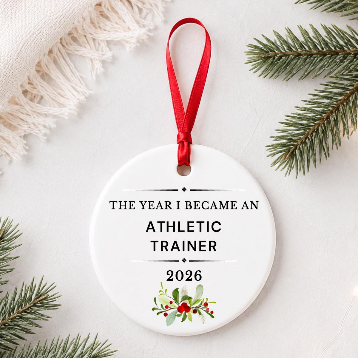 Athletic Trainer 2026 ceramic ornament reading The Year I Became an Athletic Trainer styled with pine branches on a soft white background