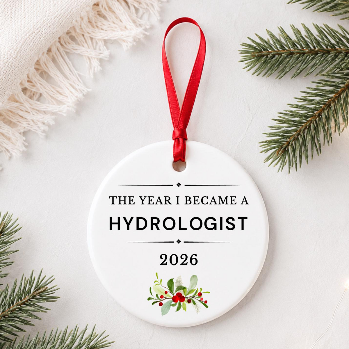 Hydrologist 2026 ceramic ornament reading The Year I Became a Hydrologist styled with pine branches on a soft white background