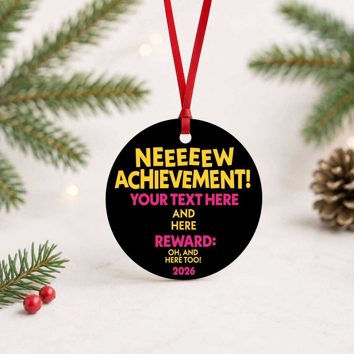 Black custom achievement ornament with yellow and pink text standing beside Christmas greenery