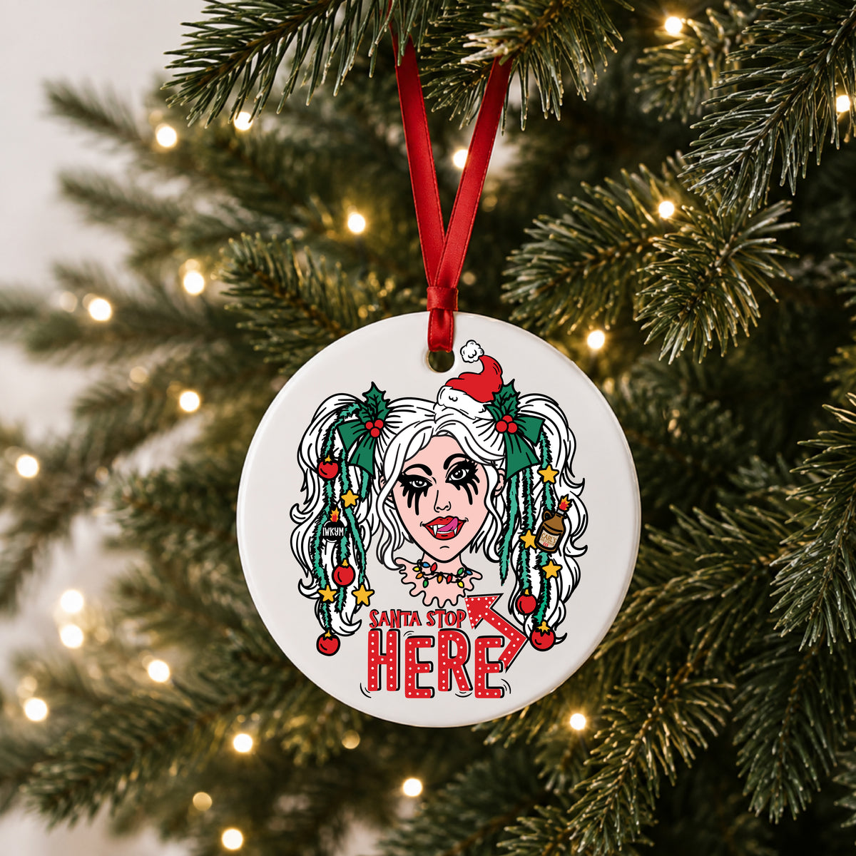 White ceramic Samantha Santa Stop Here ornament with tinsel pigtails and Santa hat hanging on a lit Christmas tree