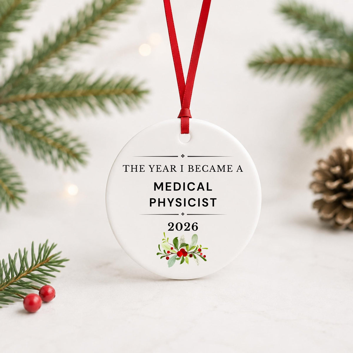 Medical Physicist 2026 ceramic ornament reading The Year I Became a Medical Physicist with red ribbon on a white surface with pine branches and pinecones