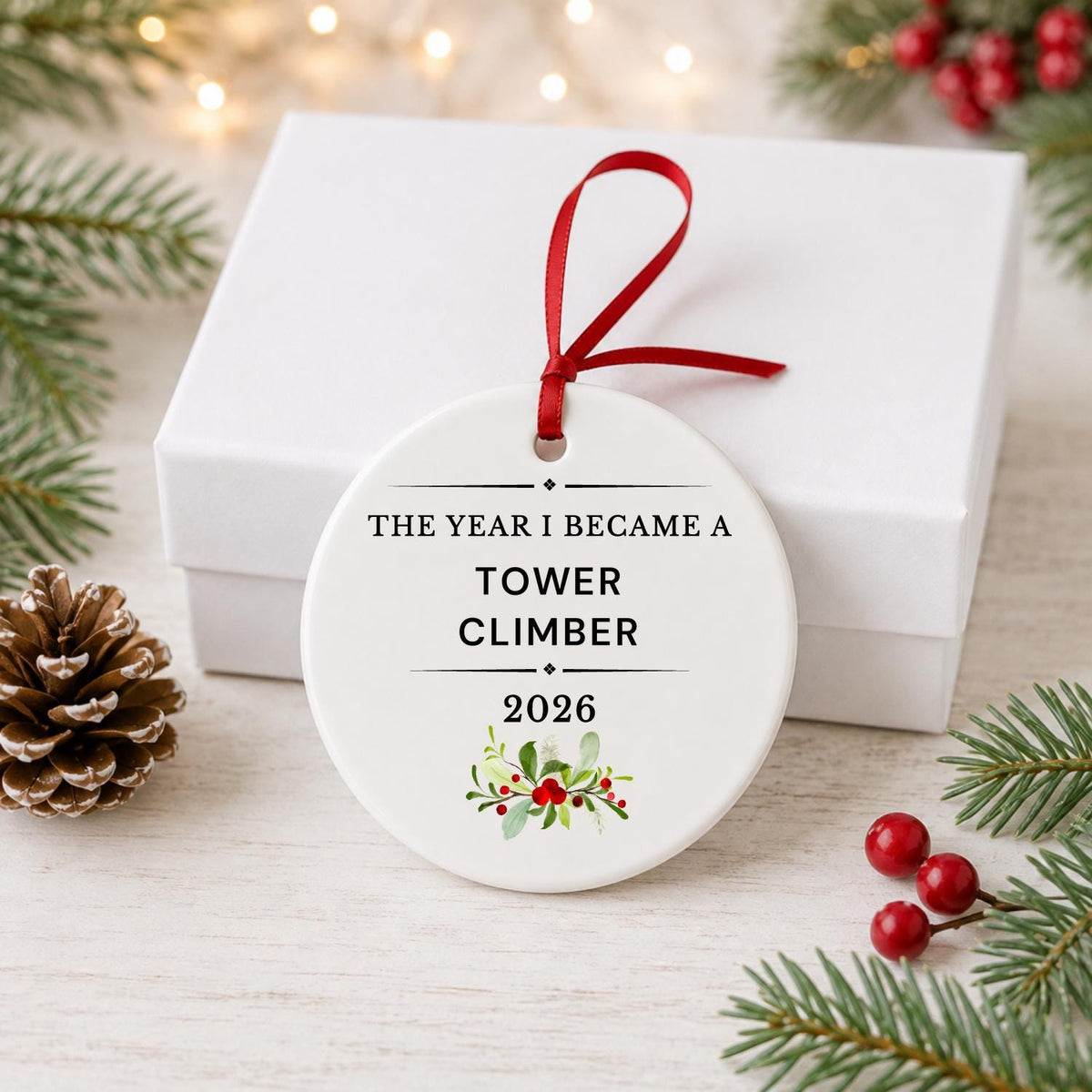 Tower Climber 2026 ceramic ornament reading The Year I Became a Tower Climber in front of a white gift box with pinecones and red berries