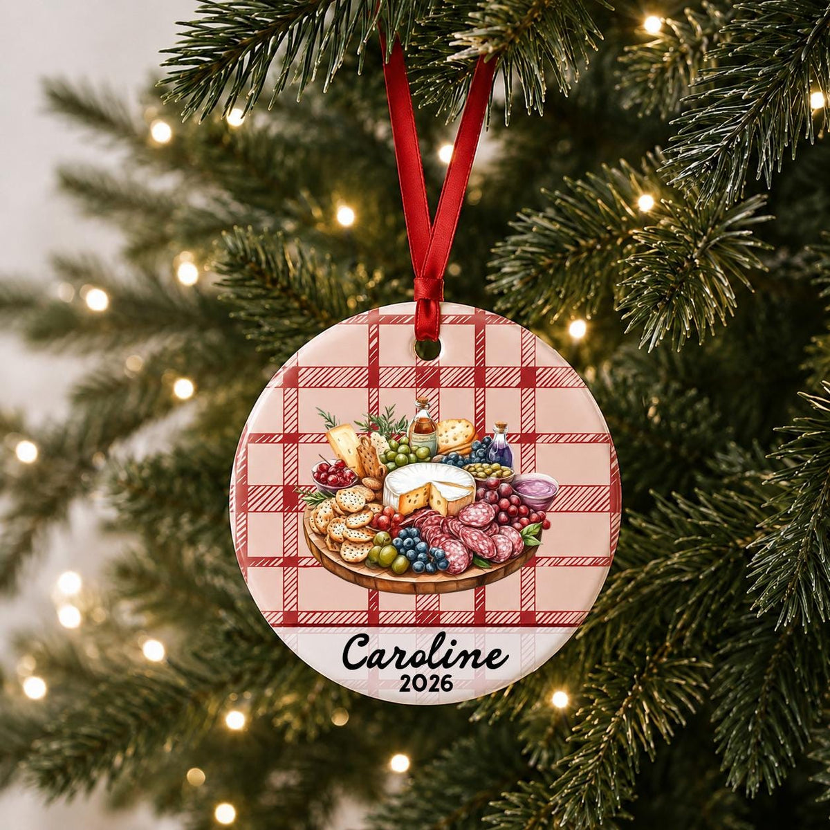 Personalized charcuterie board ceramic ornament with name and year on red plaid hanging on a lit Christmas tree