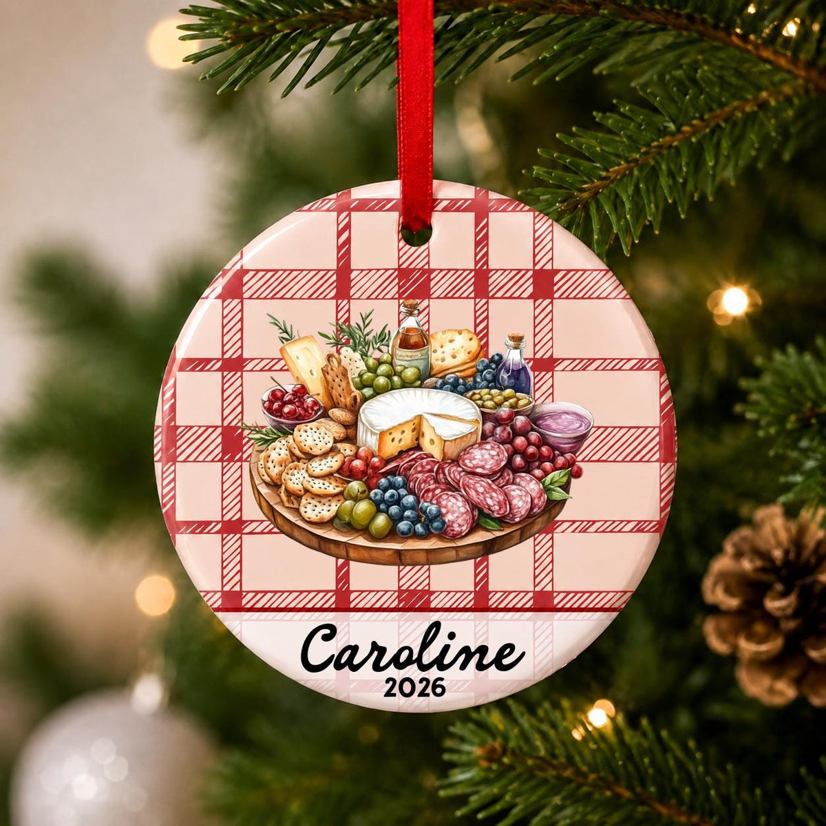 Close-up of the personalized charcuterie board ceramic ornament with name and year on red plaid hanging on a Christmas tree