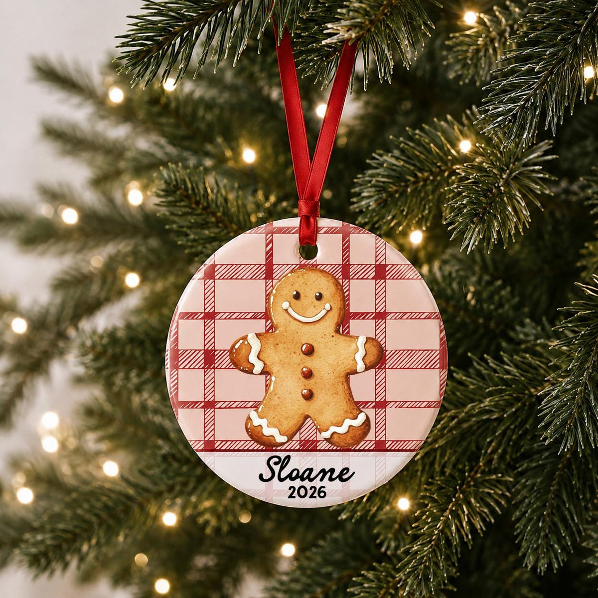 Personalized gingerbread man ceramic ornament with name and year on red plaid hanging on a lit Christmas tree