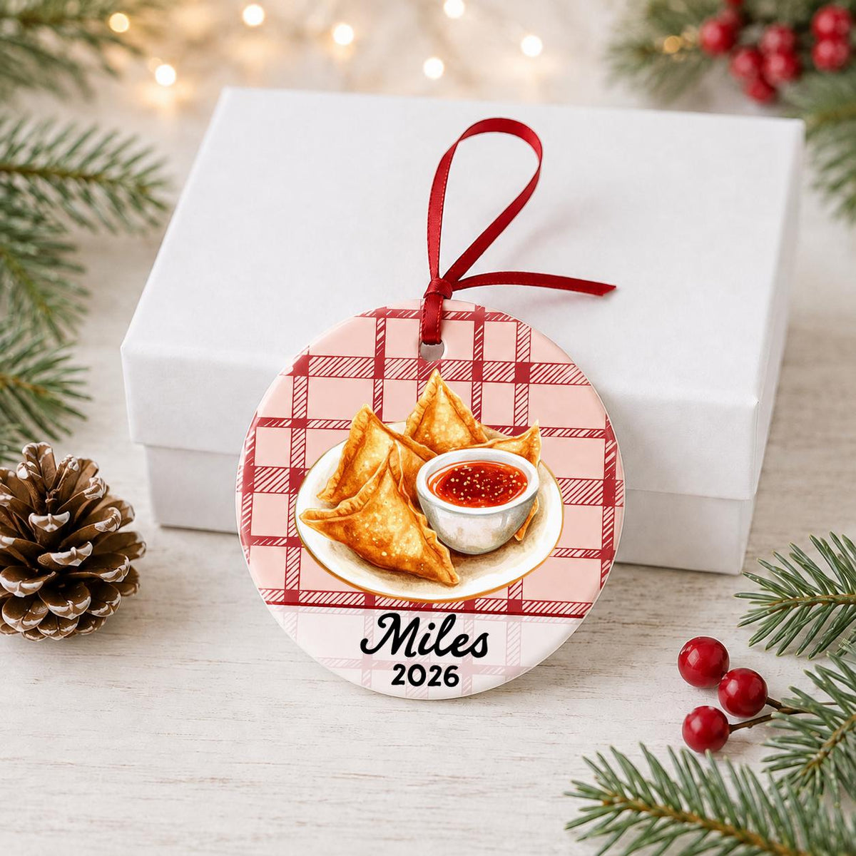 Personalized crab rangoon ceramic ornament with name and year on red plaid in front of a white gift box with pinecones and red berries