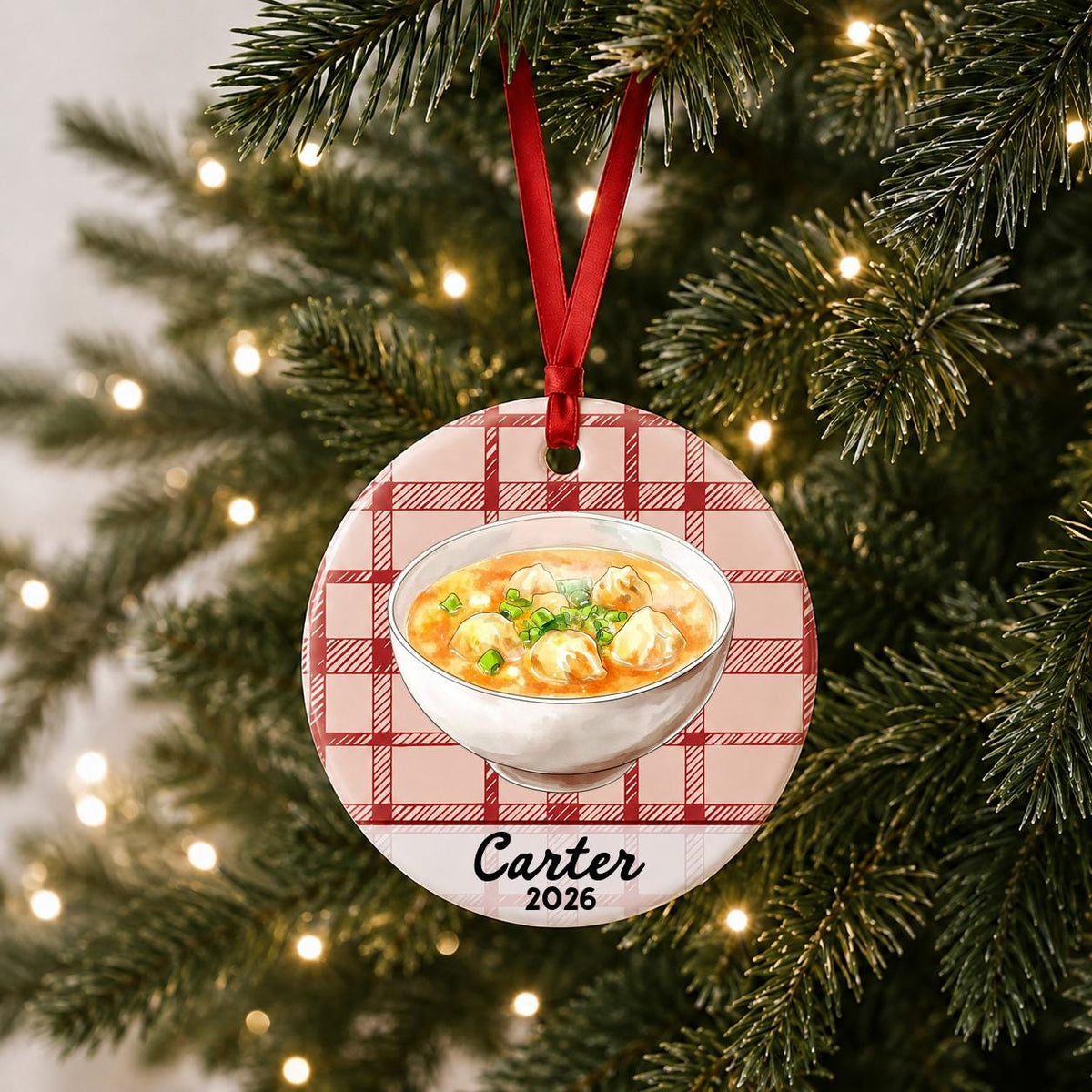 Personalized wonton soup ceramic ornament with name and year on red plaid hanging on a lit Christmas tree