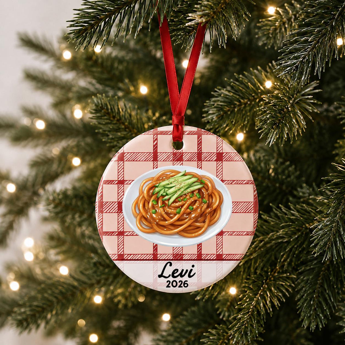 Personalized sesame noodles ceramic ornament with name and year on red plaid hanging on a lit Christmas tree
