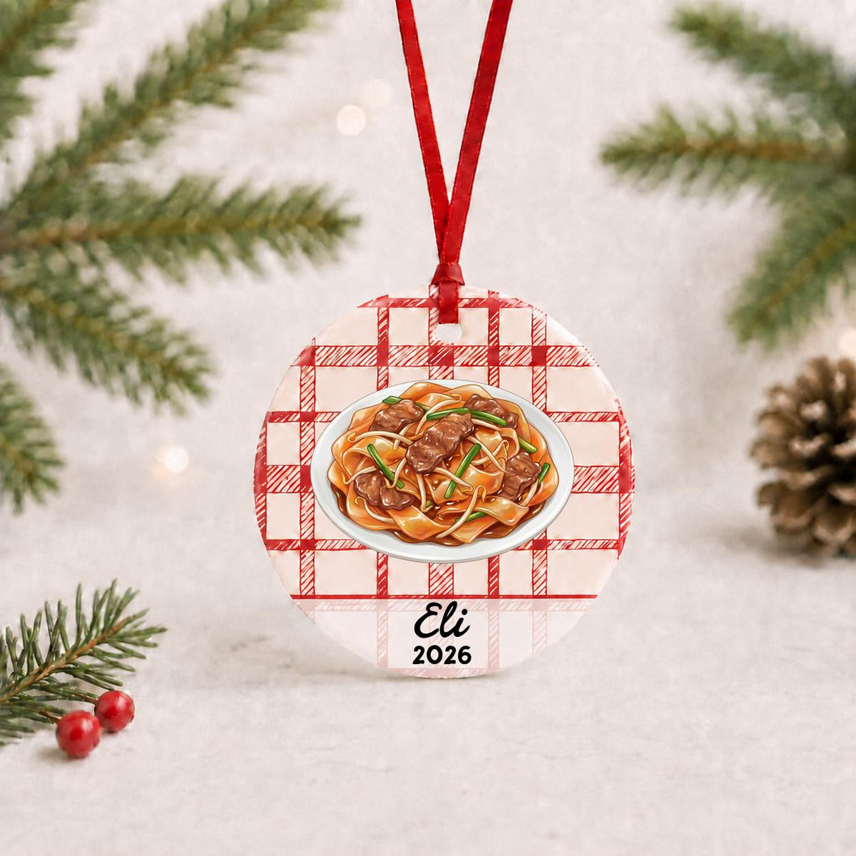 Personalized beef chow fun ceramic ornament with name and year on red plaid with red ribbon on a white surface with pine branches and pinecones