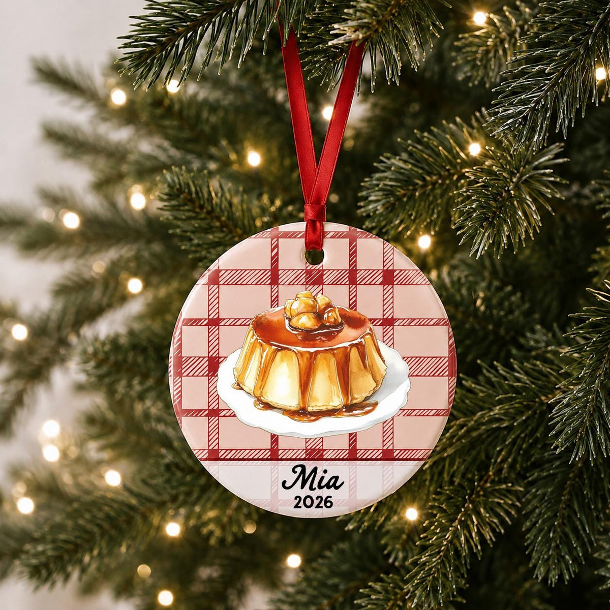 Personalized flan ceramic ornament with name and year on red plaid hanging on a lit Christmas tree