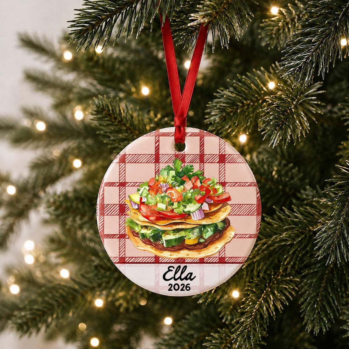 Personalized tostada ceramic ornament with name and year on red plaid hanging on a lit Christmas tree